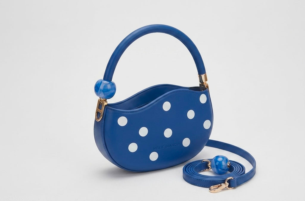 Blue handbag with white polka dots and a matching strap on a light gray background