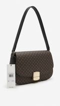 A dark brown monogram shoulder bag with a black leather strap and a gold-tone metal clasp, shown with its white Calvin Klein product tag on a clean white background.
